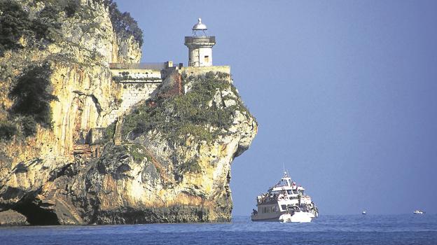 Un barco de recreo navega junto al peñón que acoge el faro de Santoña.