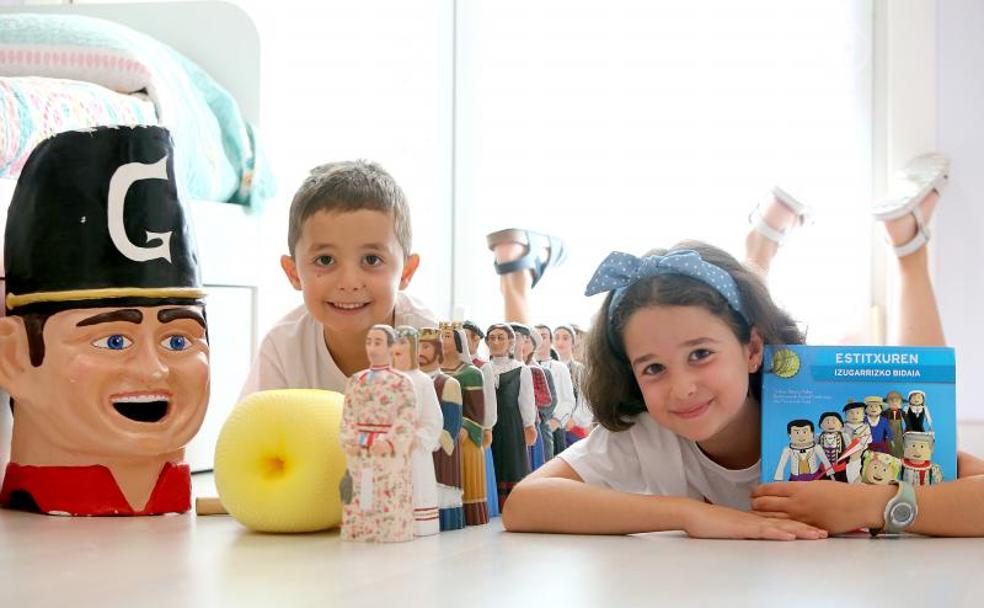 Mikel y Eider posan en la habitación de su casa con su colección de gigantes en miniatura, la cabeza de un cabezudo y un libro sobre ellos.