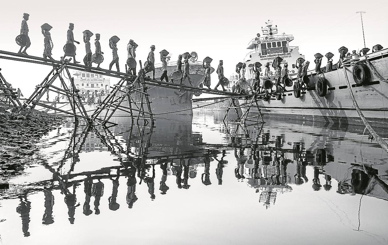 Hombres y mujeres esclavizados transportan carbón en sus cabezas en el puerto de Dhaka, en Bangladesh.