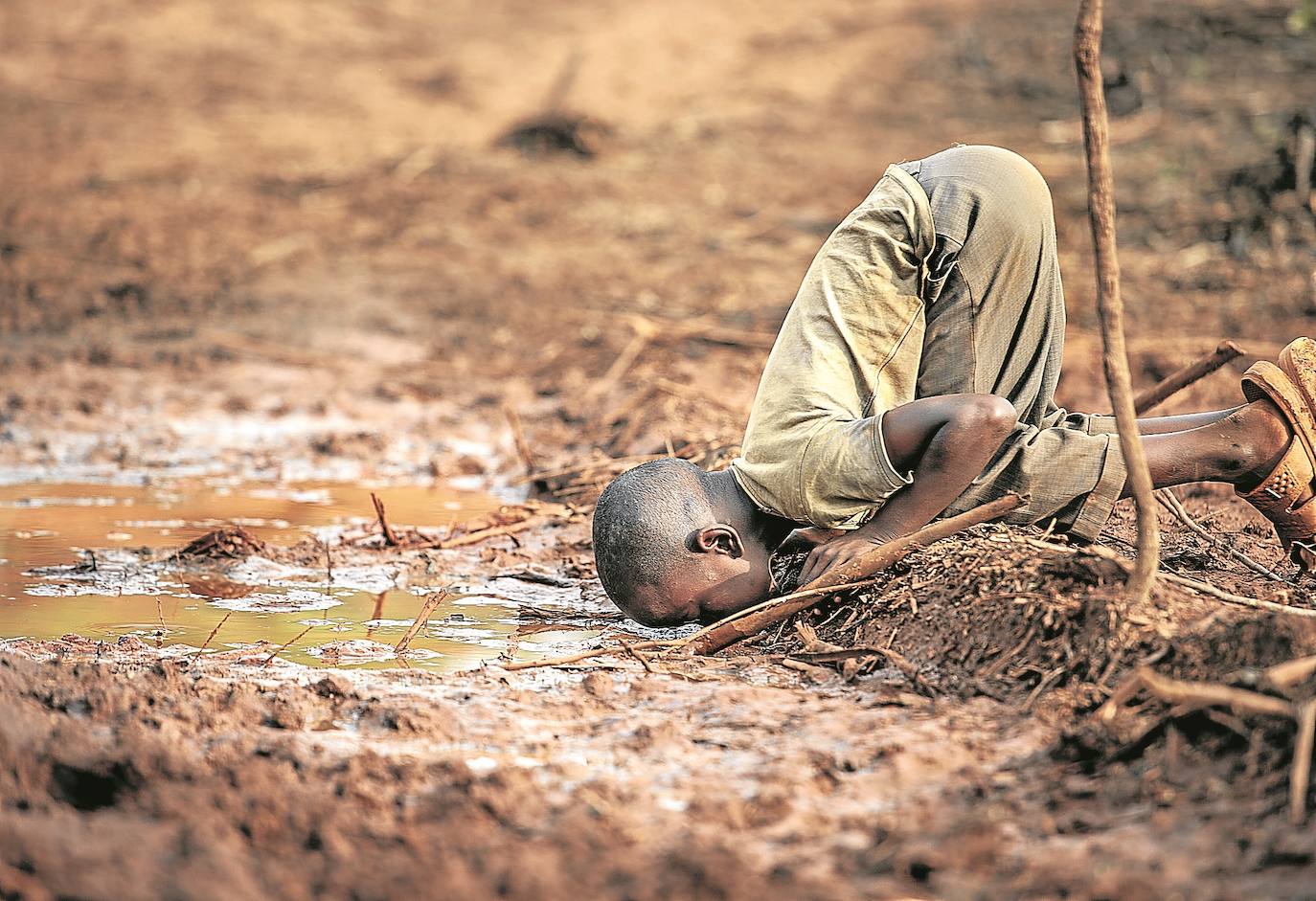 Un niño bebe agua de un charco en Kakamega, Kenia.