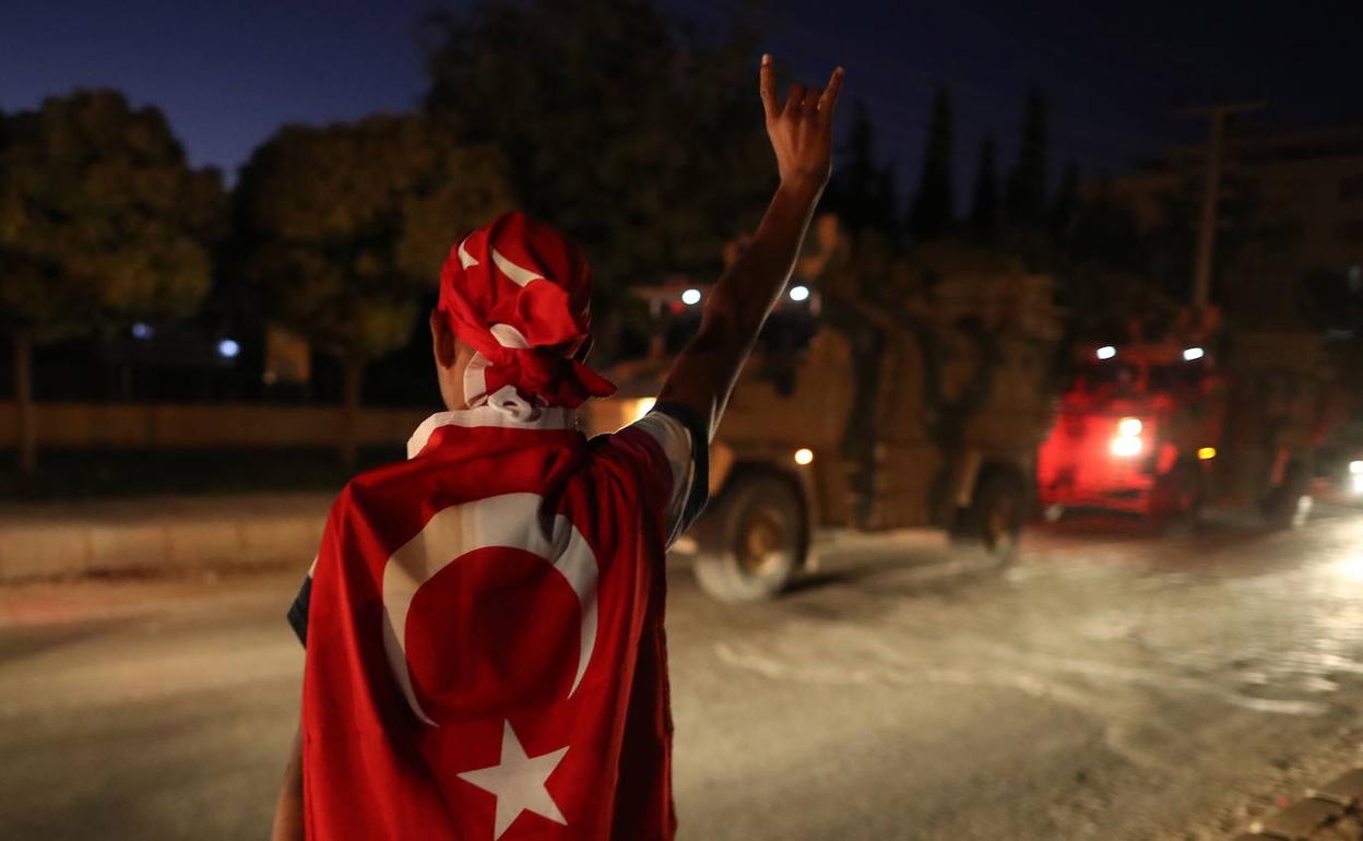 Un hombre envuelto en la bandera turca saluda a un convoy militar en la frontera con Siria.
