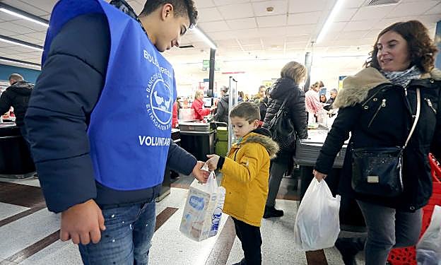 Un niño entrega una bolsa con alimentación infantil a uno de los voluntarios del centro Zabalduz Uba en el supermercado de Eroski en Arcco. 