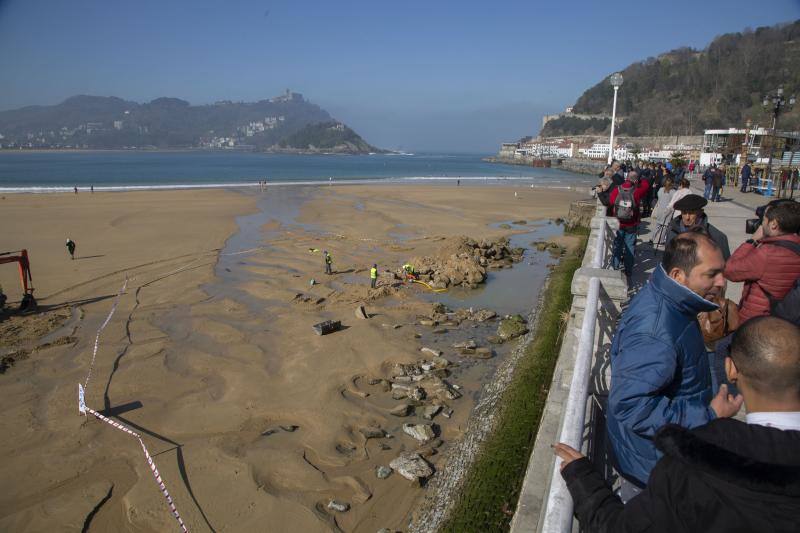 La playa de La Concha se ha convertido en la bajamar de este lunes por la mañana en un inesperado yacimiento arqueológico. La presencia de una pequeña excavadora retirando piedras y escombros junto al muro de costa a la altura del edificio consistorial ha suscitado una gran expectación entre los numerosos viandantes y turistas que han provechado el buen tiempo para dar un paseo. La máquina profundizaba en la arena en busca de los restos de un barco hundido del que hay constancia documental desde el siglo XVIII. 