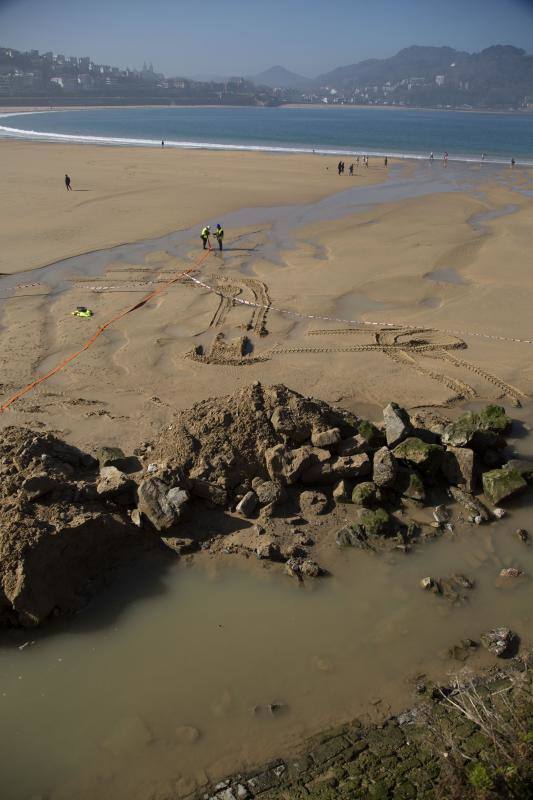 La playa de La Concha se ha convertido en la bajamar de este lunes por la mañana en un inesperado yacimiento arqueológico. La presencia de una pequeña excavadora retirando piedras y escombros junto al muro de costa a la altura del edificio consistorial ha suscitado una gran expectación entre los numerosos viandantes y turistas que han provechado el buen tiempo para dar un paseo. La máquina profundizaba en la arena en busca de los restos de un barco hundido del que hay constancia documental desde el siglo XVIII. 
