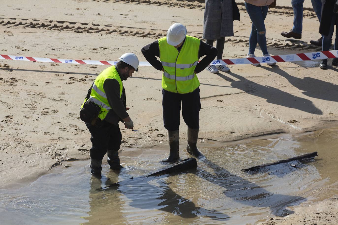 La playa de La Concha se ha convertido en la bajamar de este lunes por la mañana en un inesperado yacimiento arqueológico. La presencia de una pequeña excavadora retirando piedras y escombros junto al muro de costa a la altura del edificio consistorial ha suscitado una gran expectación entre los numerosos viandantes y turistas que han provechado el buen tiempo para dar un paseo. La máquina profundizaba en la arena en busca de los restos de un barco hundido del que hay constancia documental desde el siglo XVIII. 