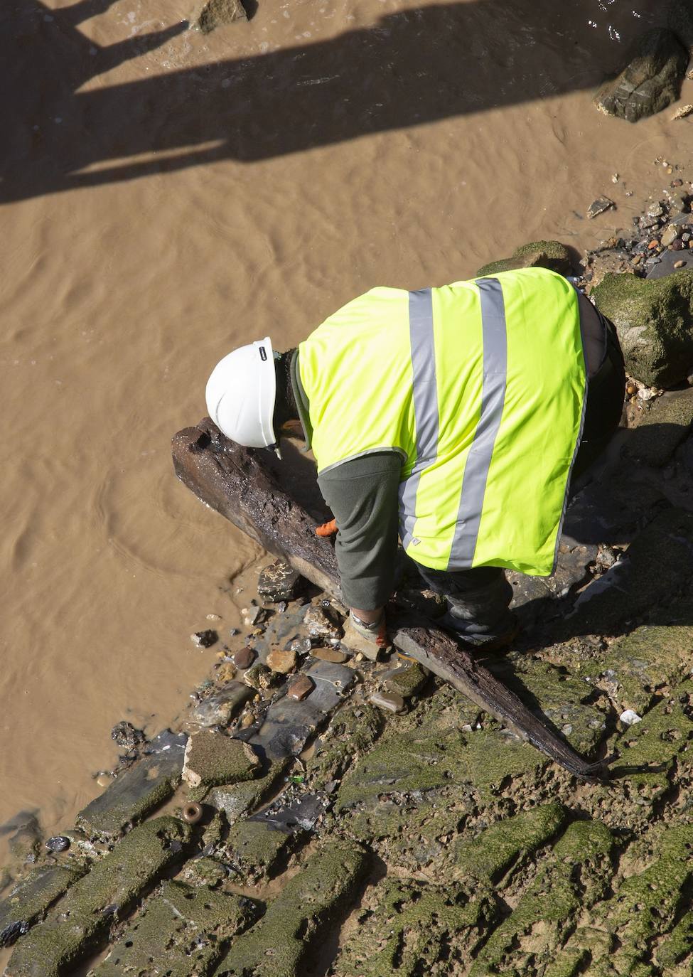La playa de La Concha se ha convertido en la bajamar de este lunes por la mañana en un inesperado yacimiento arqueológico. La presencia de una pequeña excavadora retirando piedras y escombros junto al muro de costa a la altura del edificio consistorial ha suscitado una gran expectación entre los numerosos viandantes y turistas que han provechado el buen tiempo para dar un paseo. La máquina profundizaba en la arena en busca de los restos de un barco hundido del que hay constancia documental desde el siglo XVIII. 