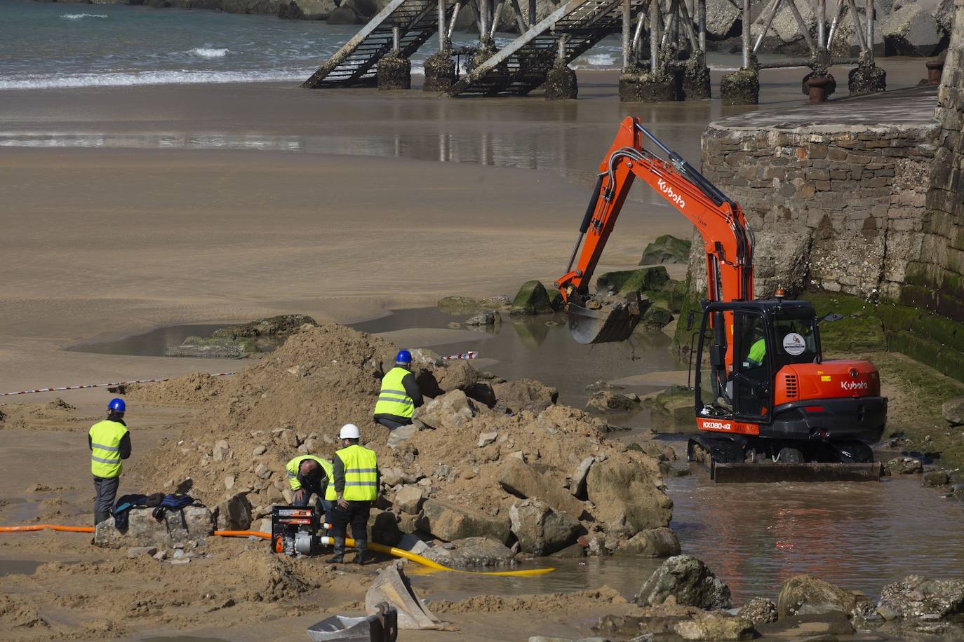 La playa de La Concha se ha convertido en la bajamar de este lunes por la mañana en un inesperado yacimiento arqueológico. La presencia de una pequeña excavadora retirando piedras y escombros junto al muro de costa a la altura del edificio consistorial ha suscitado una gran expectación entre los numerosos viandantes y turistas que han provechado el buen tiempo para dar un paseo. La máquina profundizaba en la arena en busca de los restos de un barco hundido del que hay constancia documental desde el siglo XVIII. 