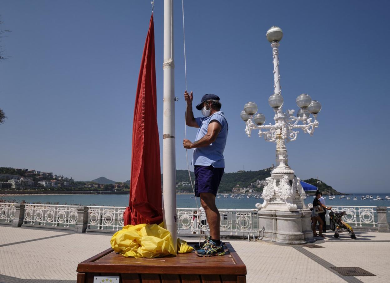 Un hondartzaina iza la bandera roja para advertir de que el aforo en La Concha está completo. 