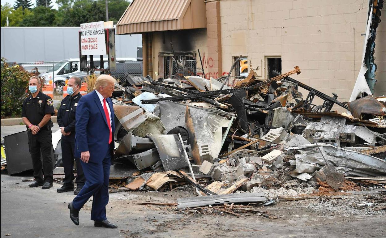 Donald Trump. sin mascarilla, observa un montón de restos de los destrozos causados durante disturbios apilados en una calle de Kenosha.