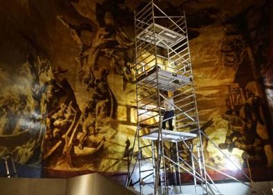 Imagen secundaria 1 - A la ziquierda: el lienzo dañado preside el ábside de la iglesia de San Telmo. A la derecha: un restaurador da los últimos toques al arreglo