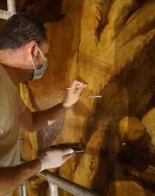 Imagen secundaria 2 - A la ziquierda: el lienzo dañado preside el ábside de la iglesia de San Telmo. A la derecha: un restaurador da los últimos toques al arreglo