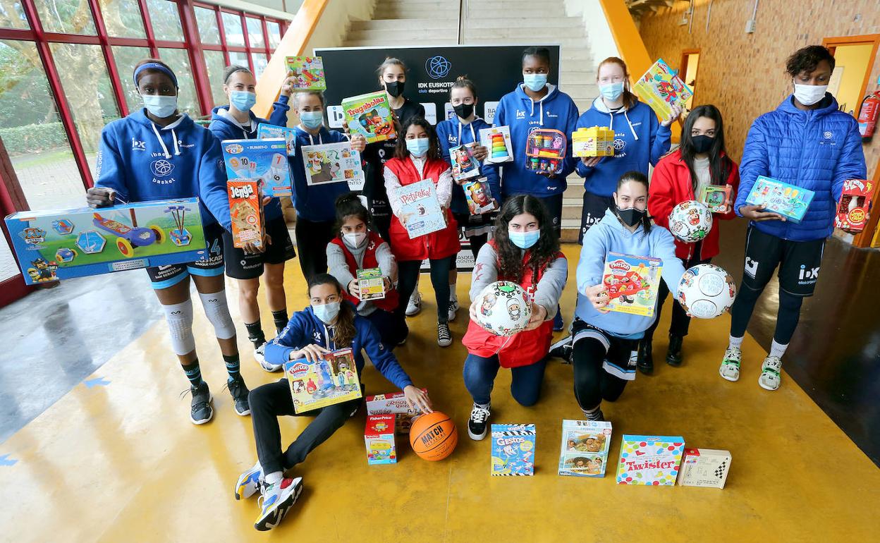 La plantilla del IDK Euskotren posa con voluntarios de la Cruz Roja y los juguetes recogidos por el club en la campaña solidaria.