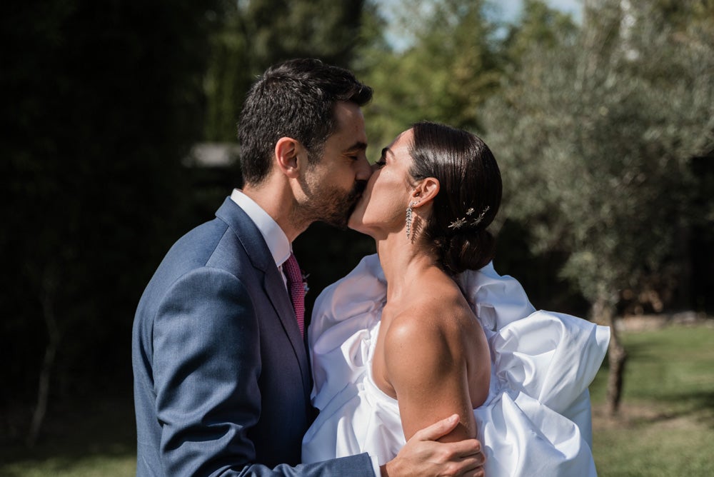 María y Jorge se casaron en Gorliz en una ceremonia íntima adaptada a las circunstancias. De largura 'mini' por encima de la rodilla, con corte asímetrico, volumen en la parte superior y lazadas laterales, la protagonista se ha convertido en una de las novias más impresionantes de las últimas semanas. El diseño lo ha firmado Fabio Encinar, uno de los diseñadores con sede en Madrid más de moda. En cuanto al peinado, otro de los elementos más destacados del estilismo, ha optado por un acertado moño bajo de bailarina súper pulido y tirante, con horquillas de Oui Novias