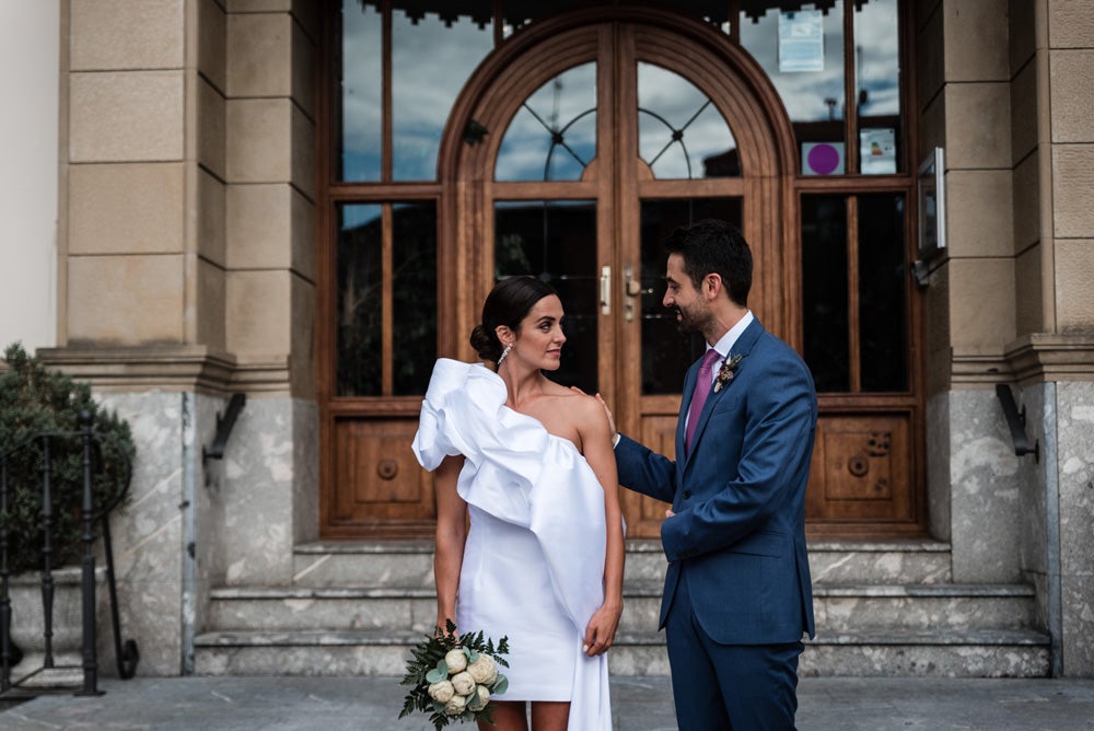 María y Jorge se casaron en Gorliz en una ceremonia íntima adaptada a las circunstancias. De largura 'mini' por encima de la rodilla, con corte asímetrico, volumen en la parte superior y lazadas laterales, la protagonista se ha convertido en una de las novias más impresionantes de las últimas semanas. El diseño lo ha firmado Fabio Encinar, uno de los diseñadores con sede en Madrid más de moda. En cuanto al peinado, otro de los elementos más destacados del estilismo, ha optado por un acertado moño bajo de bailarina súper pulido y tirante, con horquillas de Oui Novias