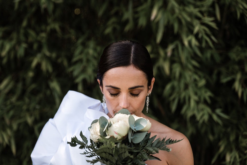 María y Jorge se casaron en Gorliz en una ceremonia íntima adaptada a las circunstancias. De largura 'mini' por encima de la rodilla, con corte asímetrico, volumen en la parte superior y lazadas laterales, la protagonista se ha convertido en una de las novias más impresionantes de las últimas semanas. El diseño lo ha firmado Fabio Encinar, uno de los diseñadores con sede en Madrid más de moda. En cuanto al peinado, otro de los elementos más destacados del estilismo, ha optado por un acertado moño bajo de bailarina súper pulido y tirante, con horquillas de Oui Novias