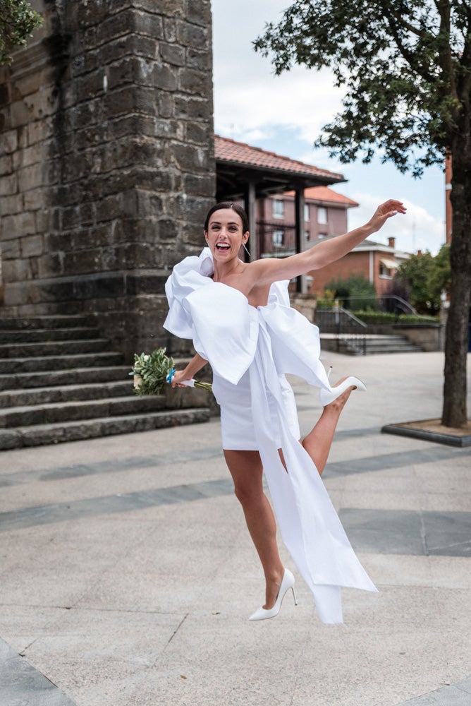 María y Jorge se casaron en Gorliz en una ceremonia íntima adaptada a las circunstancias. De largura 'mini' por encima de la rodilla, con corte asímetrico, volumen en la parte superior y lazadas laterales, la protagonista se ha convertido en una de las novias más impresionantes de las últimas semanas. El diseño lo ha firmado Fabio Encinar, uno de los diseñadores con sede en Madrid más de moda. En cuanto al peinado, otro de los elementos más destacados del estilismo, ha optado por un acertado moño bajo de bailarina súper pulido y tirante, con horquillas de Oui Novias