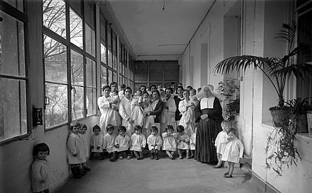 Imagen principal - Nodrizas, madres e Hijas de la Caridad con el director Jesús Alústiza. Para evitar abandonos en la vía pública o infanticidios, crearon estos cilindros giratorios. Desde el exterior la madre colocaba al bebé, el torno giraba y activaba una alarma para que la criatura fuera recogida en el interior. Hubo en Donostia, Tolosa, Azpeitia y Bergara.