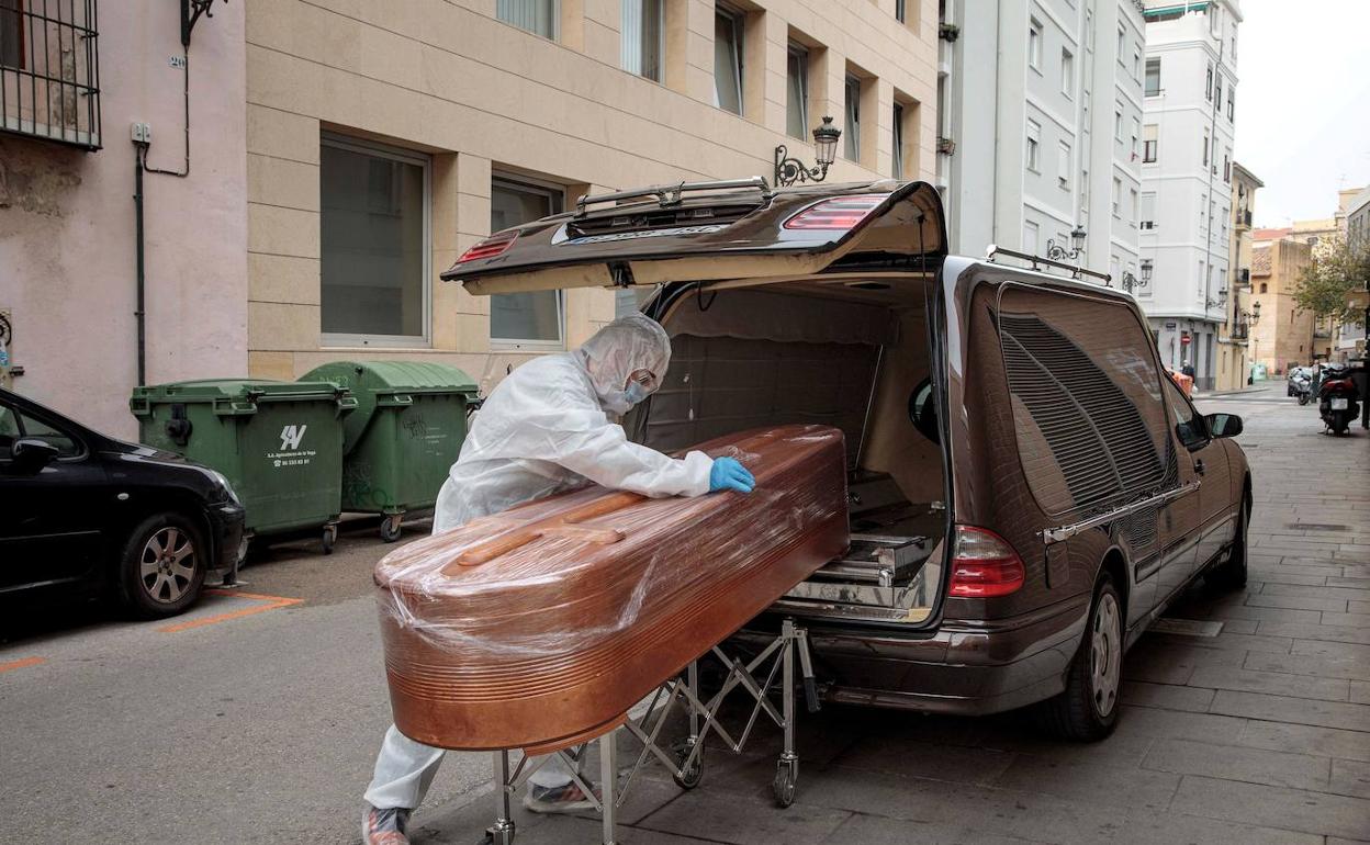 Un operario de una funeraria introduce un féretro en el vehículo. 