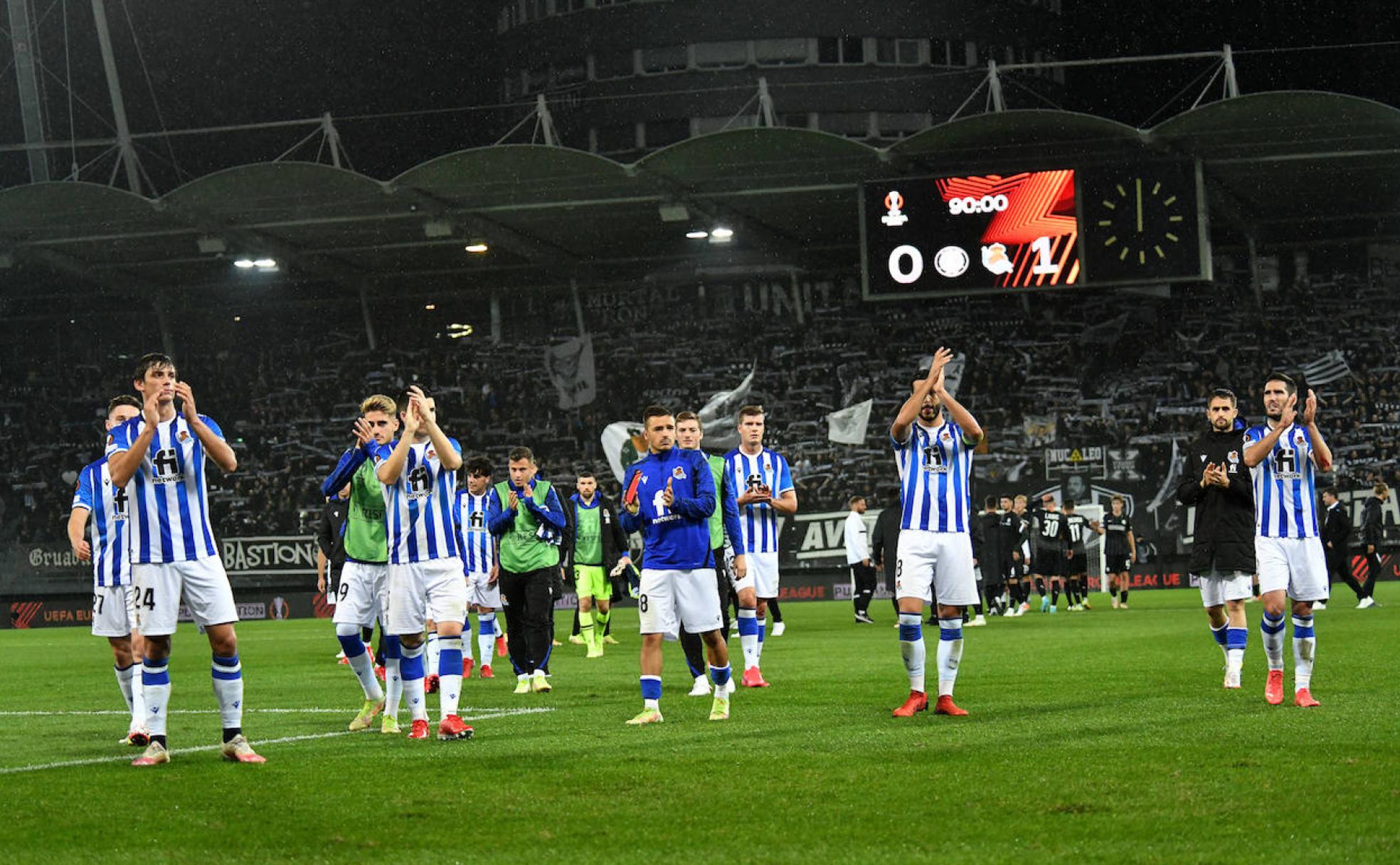Los jugadores aplauden a la afición a la conclusión del partido, con el marcador que refleja el triunfo, detrás.