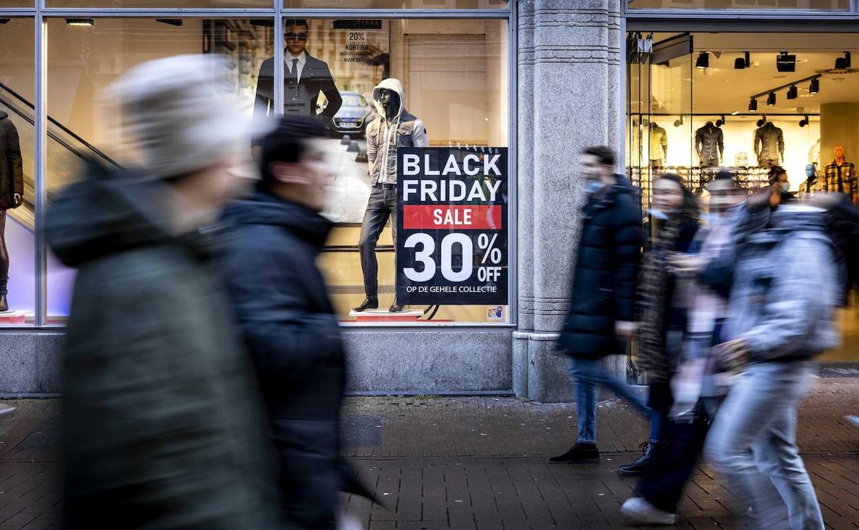 La gente pasea frente a los escaparates con los carteles de las rebajas por el Black Friday