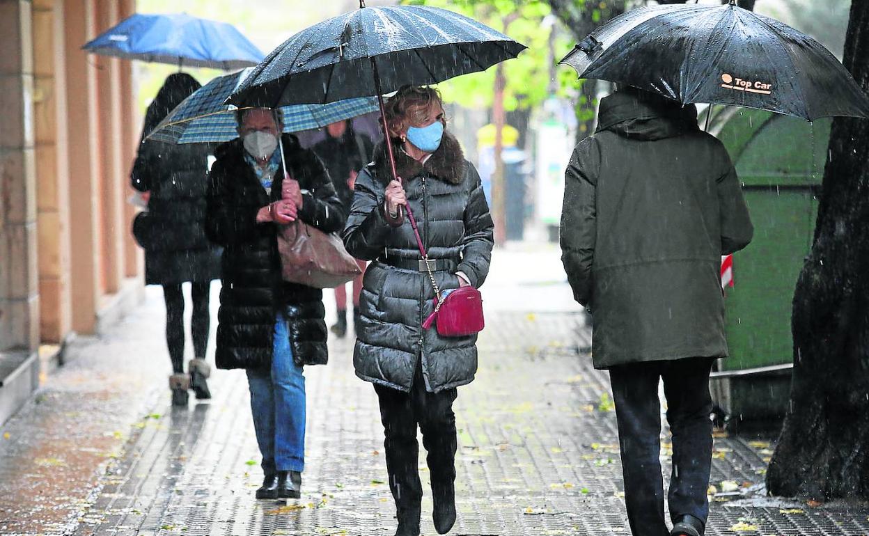 Varias personas se protegen deoblemente con paraguas y mascarillas durante estos días en los que arrecian la lluvia y los contagios.