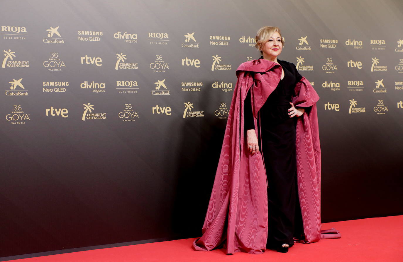 Carmen Machi ha sido una de las actrices más rompedoras y atrevidas de la alfombra roja con un vestido largo en negro con escote en pico y una capa XXL en fucsia. Ella ha dado la bienvenida a la gala tras el espectáculo musical inicial, ya sin la capa