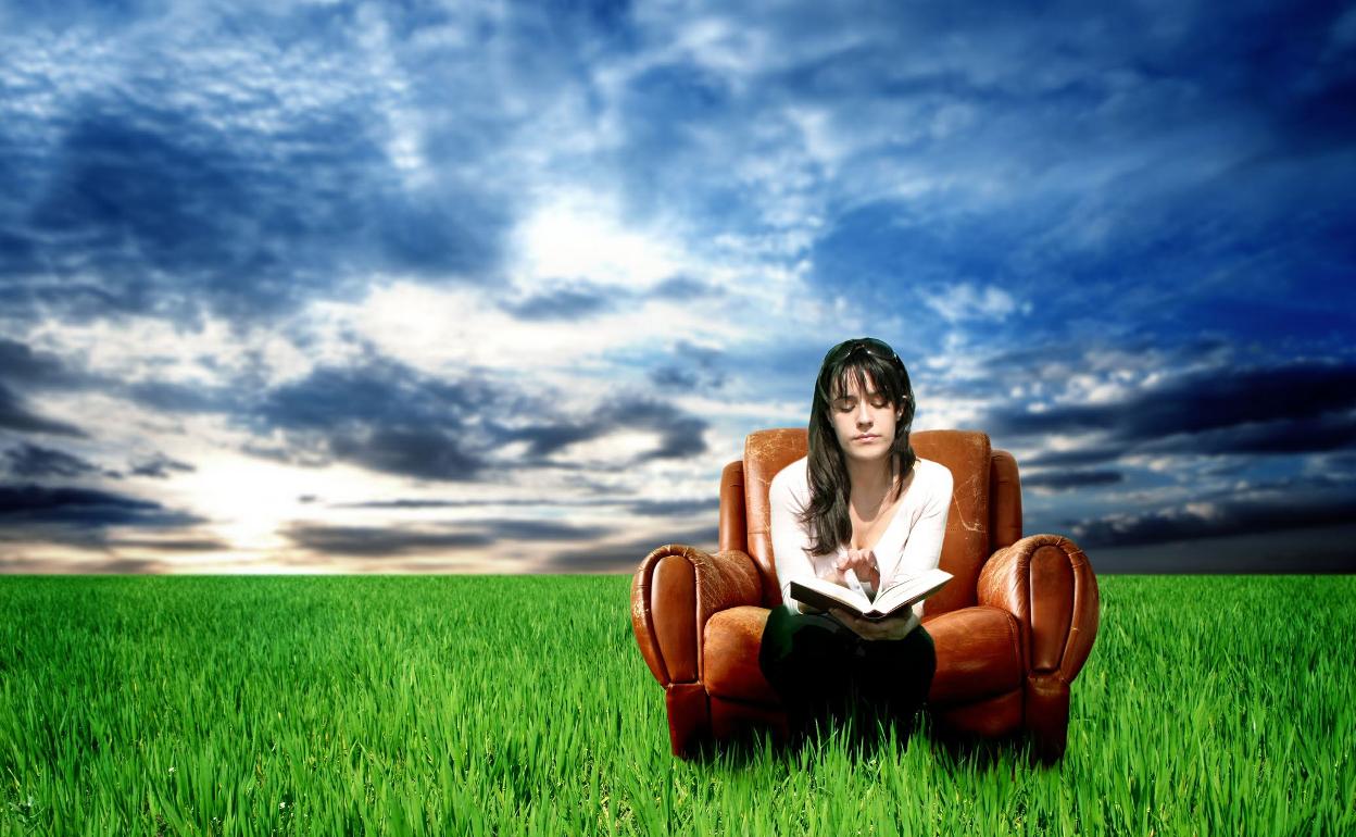 Una joven sentada en un sofá en mitad del campo con un libro. No es meditar, pero casi. 