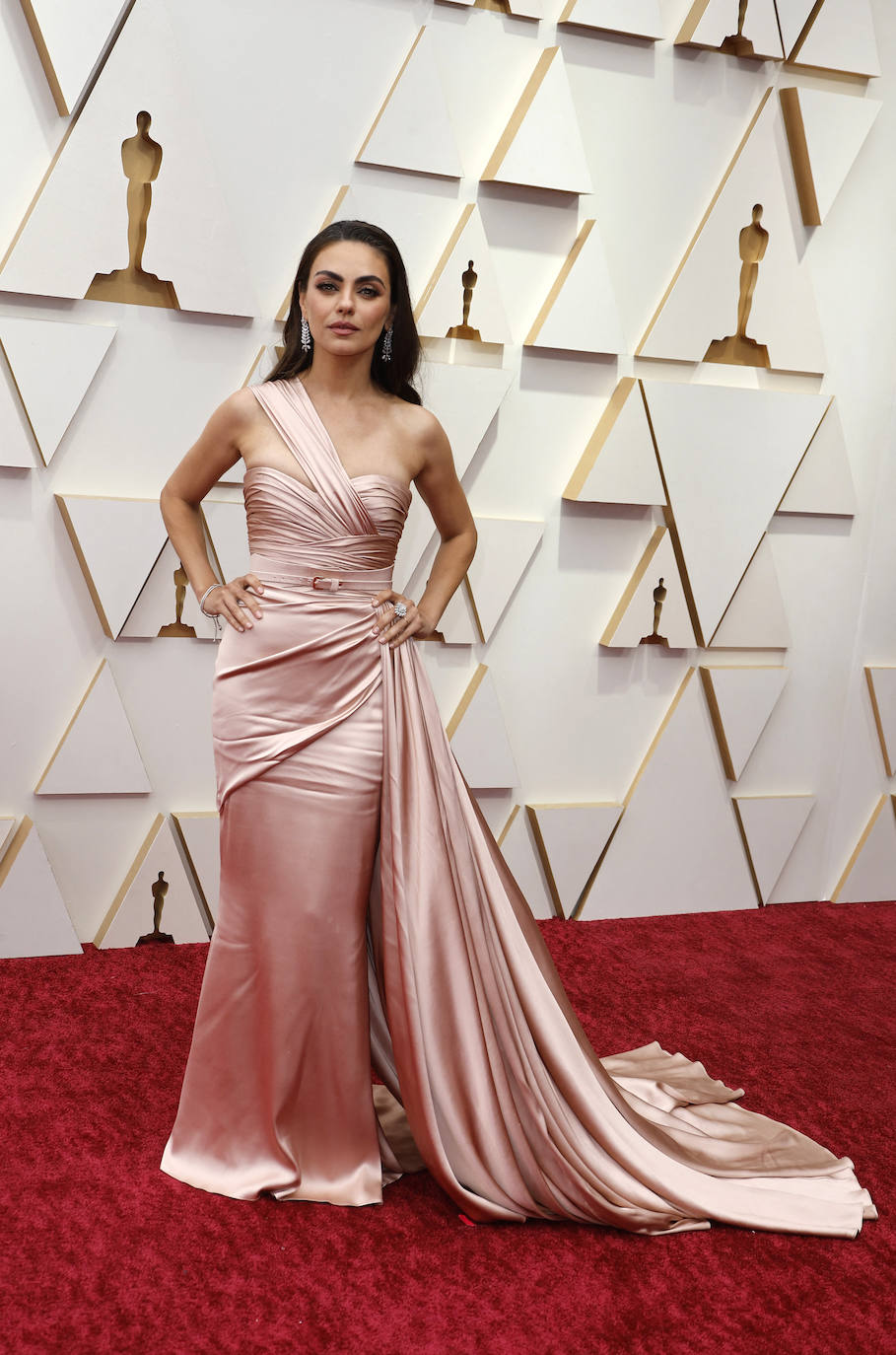 Mila Kunis ha apostado por un vestido asimétrico drapeado, con un fino cinturón al tono y cola en rosa palo. Un diseño firmado por el libanés Zuhair Murad