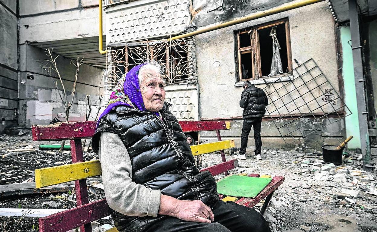 Una mujer sentada en un banco delante de un edificio completamente destruido en Járkov.