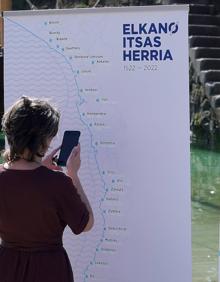 Imagen secundaria 2 - Irurzun, Olano, Agote y Alberdi en la presentación de la travesía en el muelle donostiarra.. Los remeros. Una mujer en el cartel anunciador.