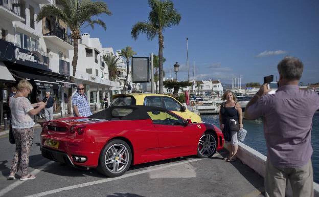 Turistas se sacan fotos delante de un coche de lujo en Puerto Banús. 