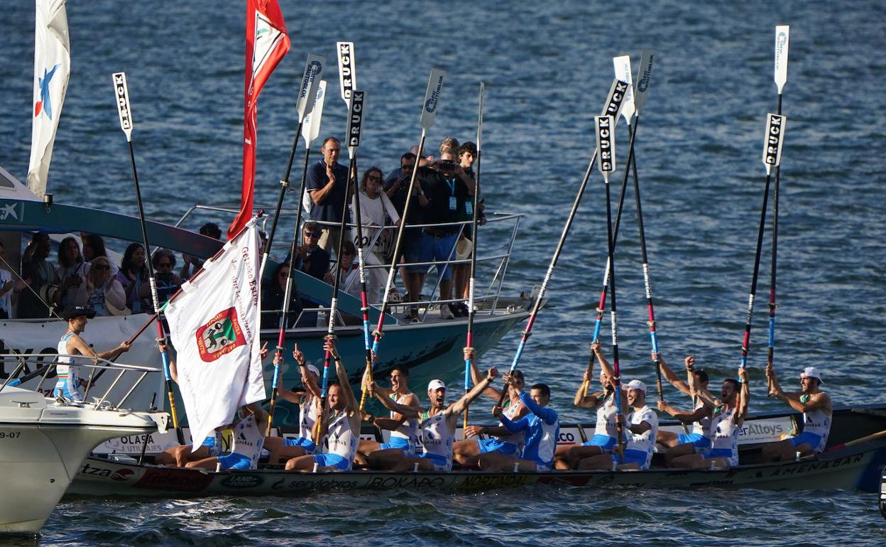 Arkaitz Díaz muestra la bandera conquistada en Getxo mientras los remeros celebran la victoria. 