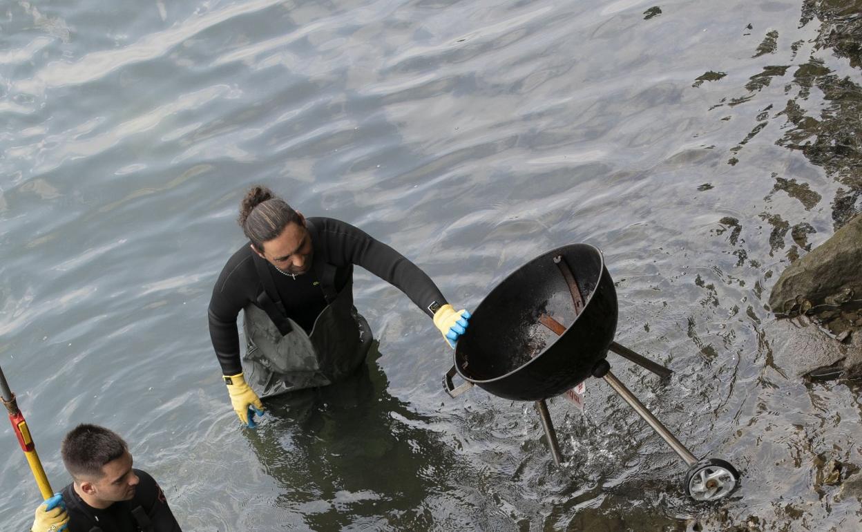Dos trabajadores del servicio de limpieza extraen una barbacoa del fondo del Urumea. 