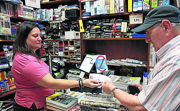 Nerea Ispura da a un cliente el TicketBai y un ejemplar de DVen su tienda de El Antiguo, en Donostia.