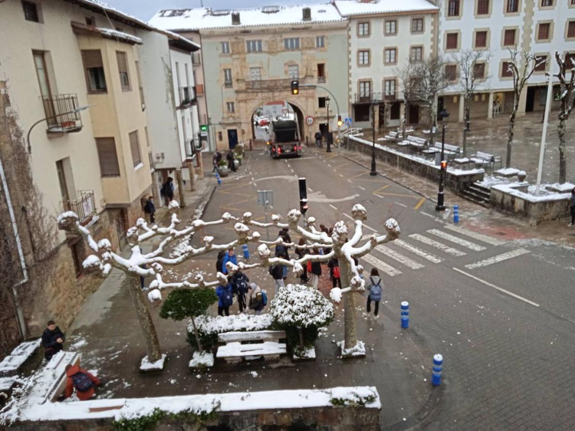 Un grupo de escolares espera al autobús con rastros de nieve todavía en el mobiliario urbano.