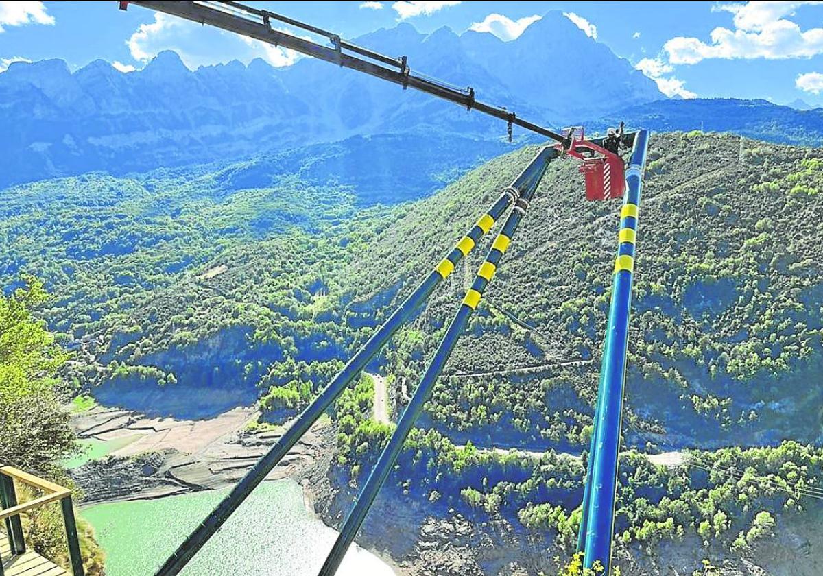 Operarios trabajan en la instalación del columpio, con el pantano de Búbal debajo y la Peña Telera reinando en el horizonte. Espectacular.