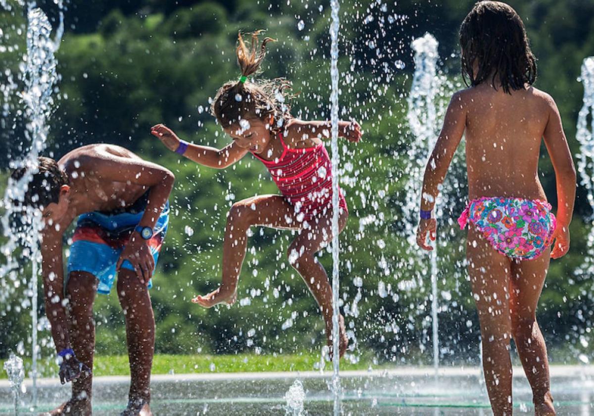 Tres menores disfrutan jugando en unos chorros de agua.