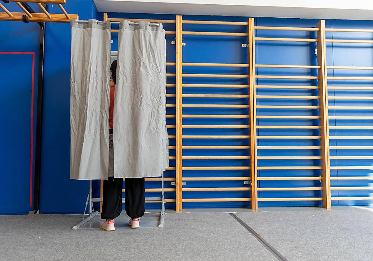 Una mujer elige sus votos en una cabina instalada en un colegio vasco.