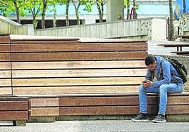 Un hombre consulta su teléfono móvil en un banco público de Usurbil.