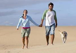 Una pareja camina por la playa junto a la compañía de su perro.