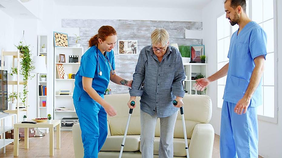 Dos enfermeros ayudan a una mujer usuaria de una residencia.