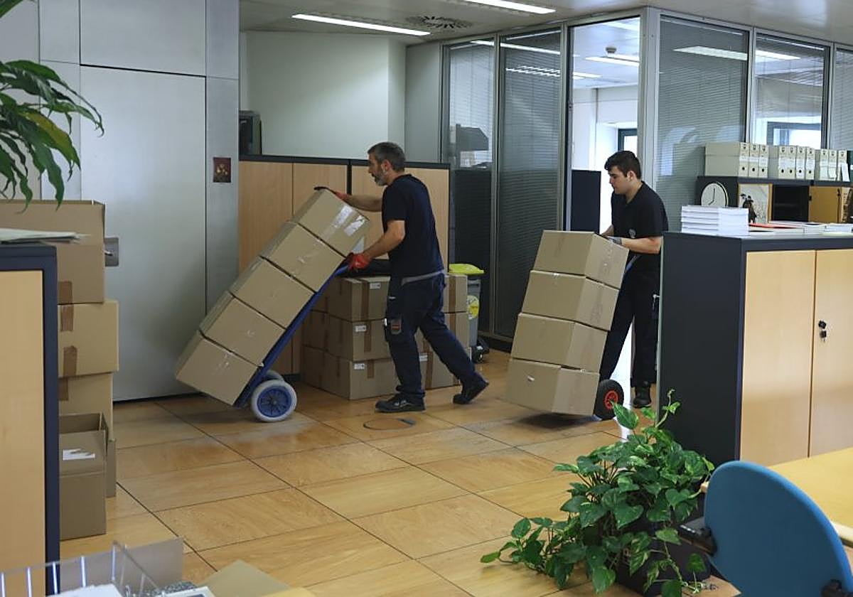 Varios operarios recogen las cajas que se acumulan en las oficinas del centro para su traslado. p
