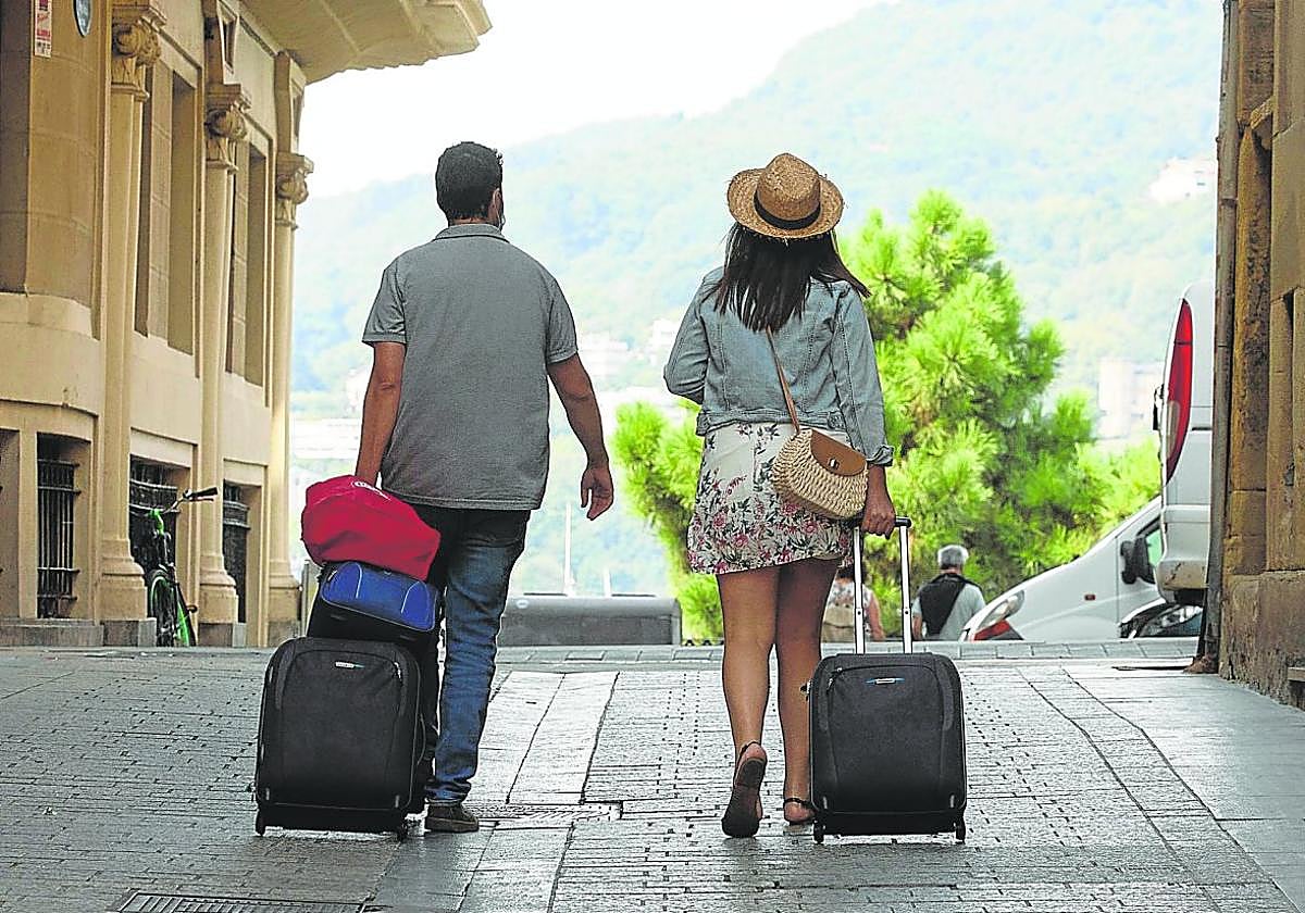 Dos turistas ajenos a la información pasean con sus maletas por la Parte Vieja de San Sebastián.
