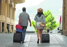 Dos turistas ajenos a la información pasean con sus maletas por la Parte Vieja de San Sebastián.