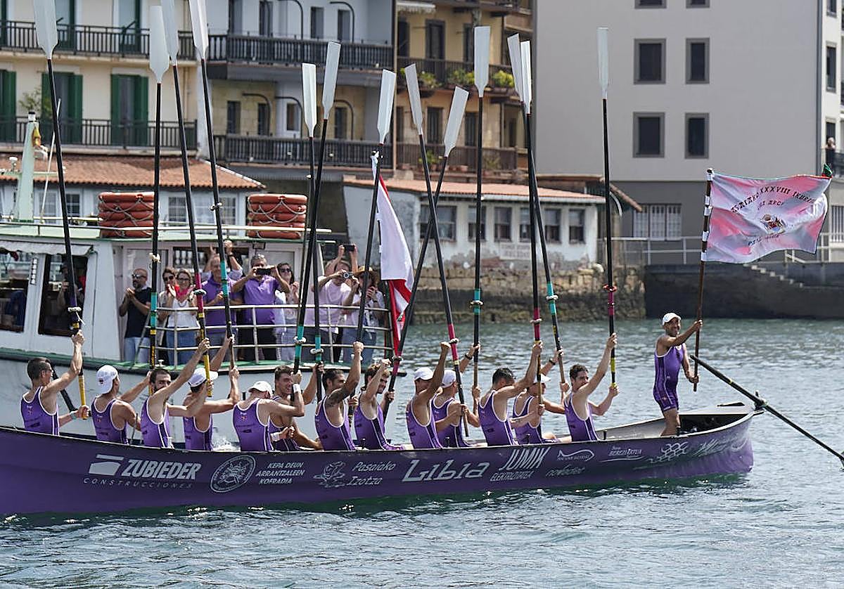 Los remeros de San Pedro levantan los remos y su patrón ondea la bandera ganada en aguas de Pasaia.