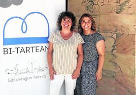 Nerea Mendizabal y Gorane Domínguez al pie del logo que representa la unión de los comerciantes de Bi-Tartean.