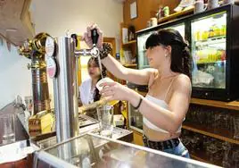 Una camarera en la barra de un bar sirviendo unas cervezas.