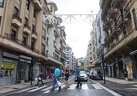 Varios peatones cruzan la carretera bajo los adornos navideños.