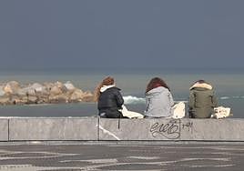 Tres jóvenes sentadas frente a la playa de La Zurriola.