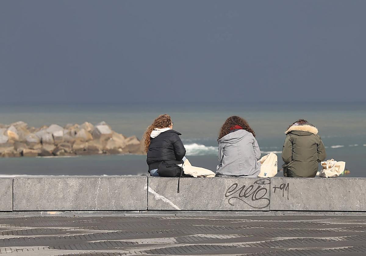Tres jóvenes sentadas frente a la playa de La Zurriola.